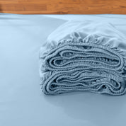 Folded fitted sheet on a bed with a wooden headboard.