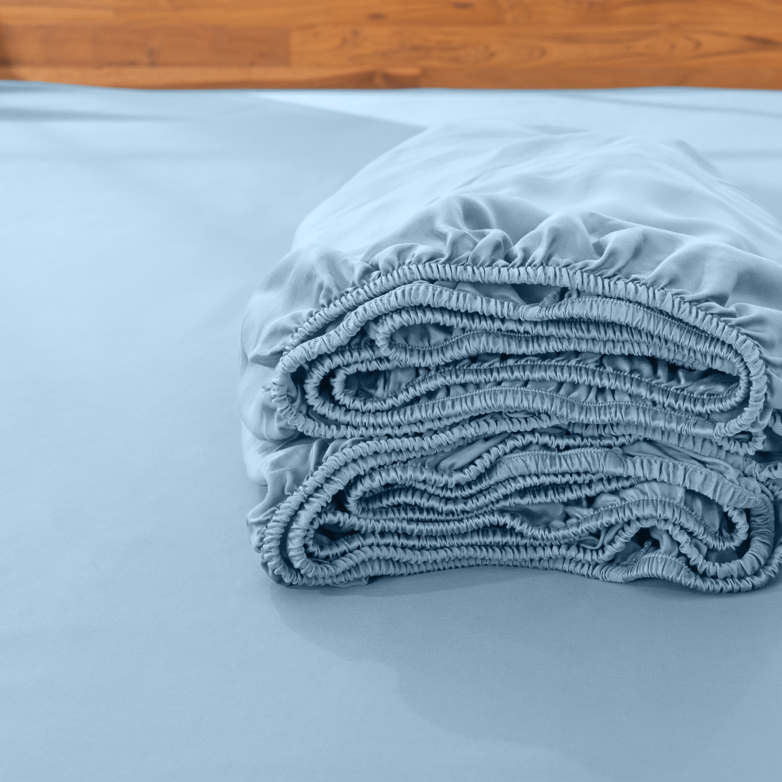 Folded fitted sheet on a bed with a wooden headboard.