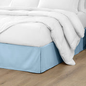 The corner of a bed with a bed skirt and comforter on it