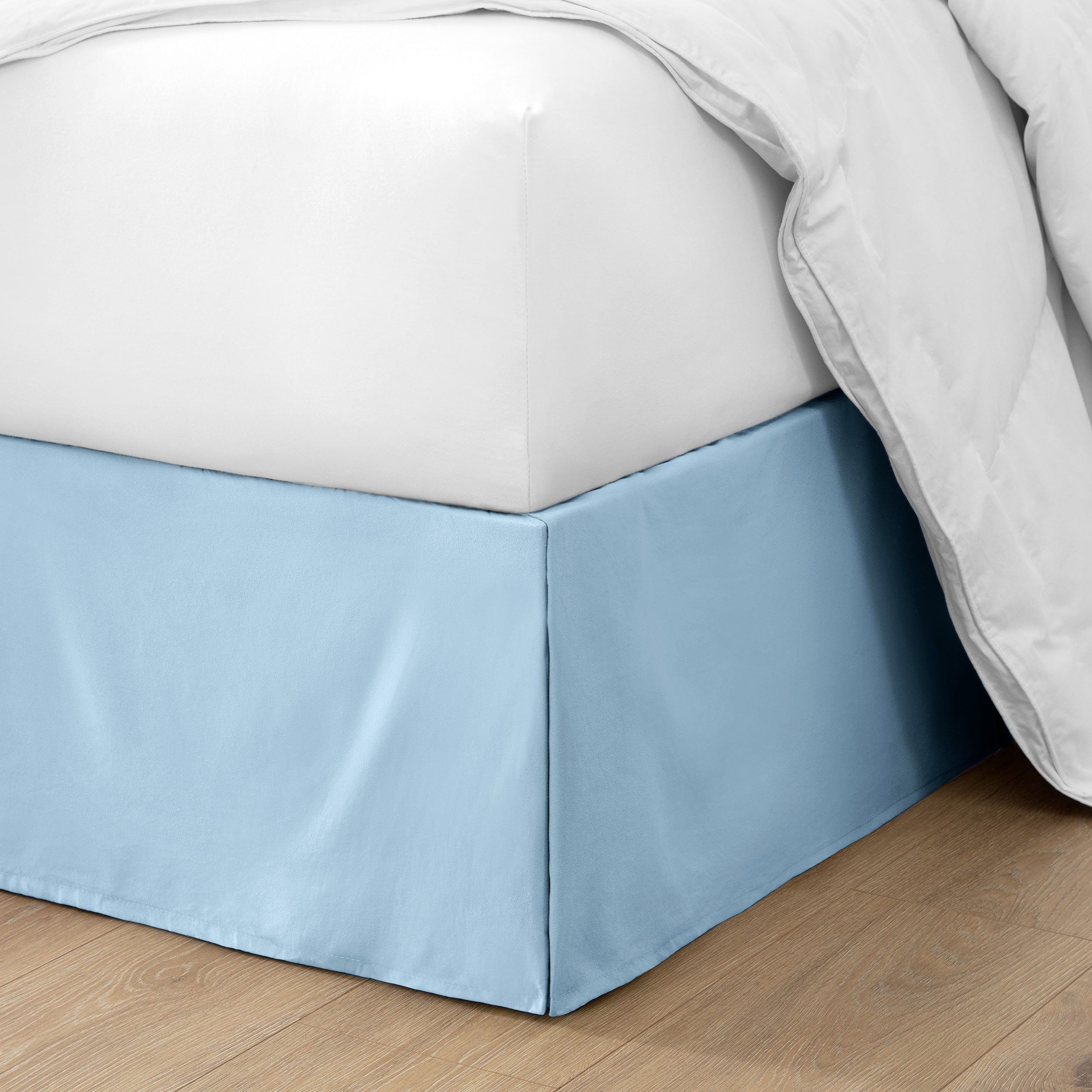 The corner of a bed with a bed skirt and comforter on it