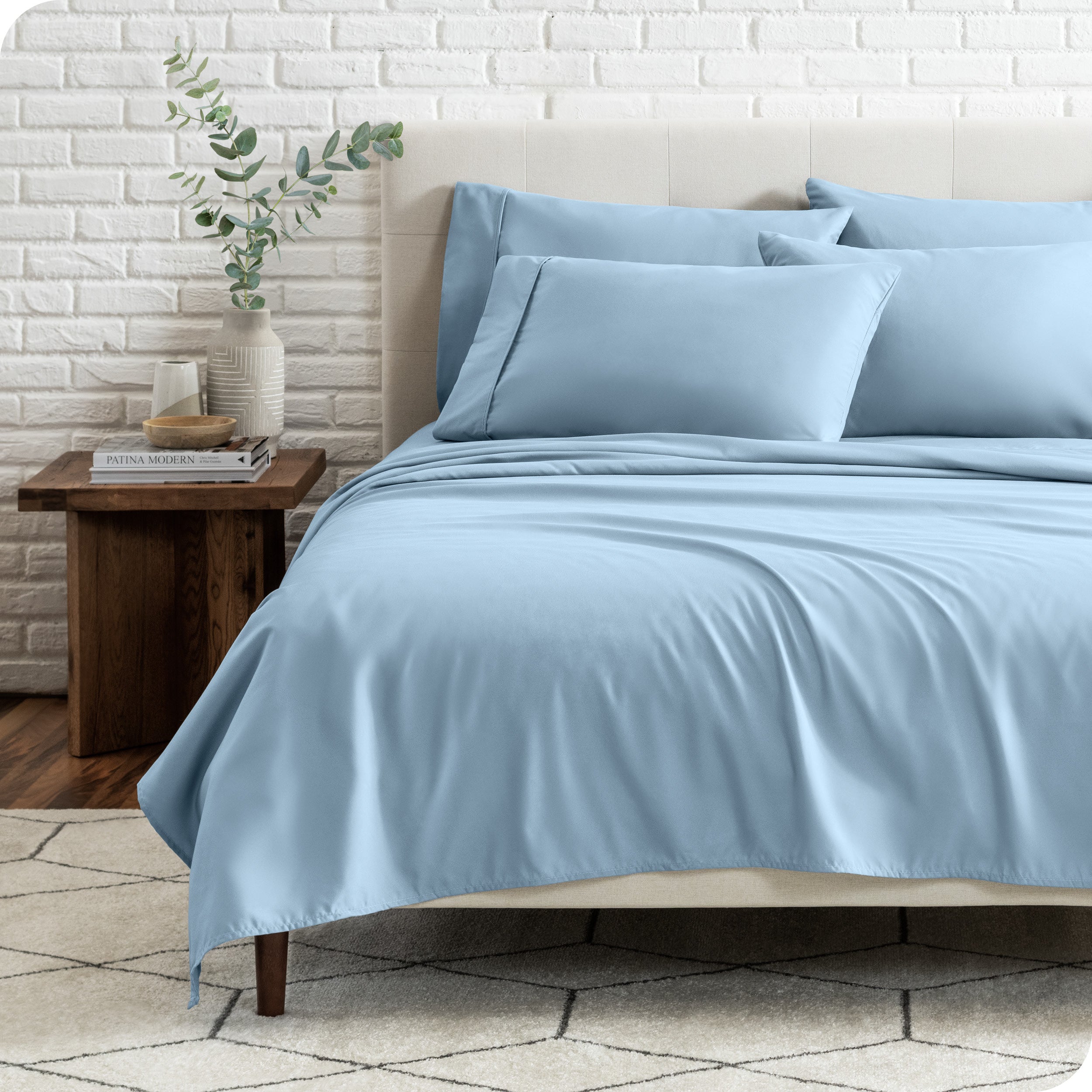 End view of a modern bed with the microfiber sheets on the bed with four pillows.