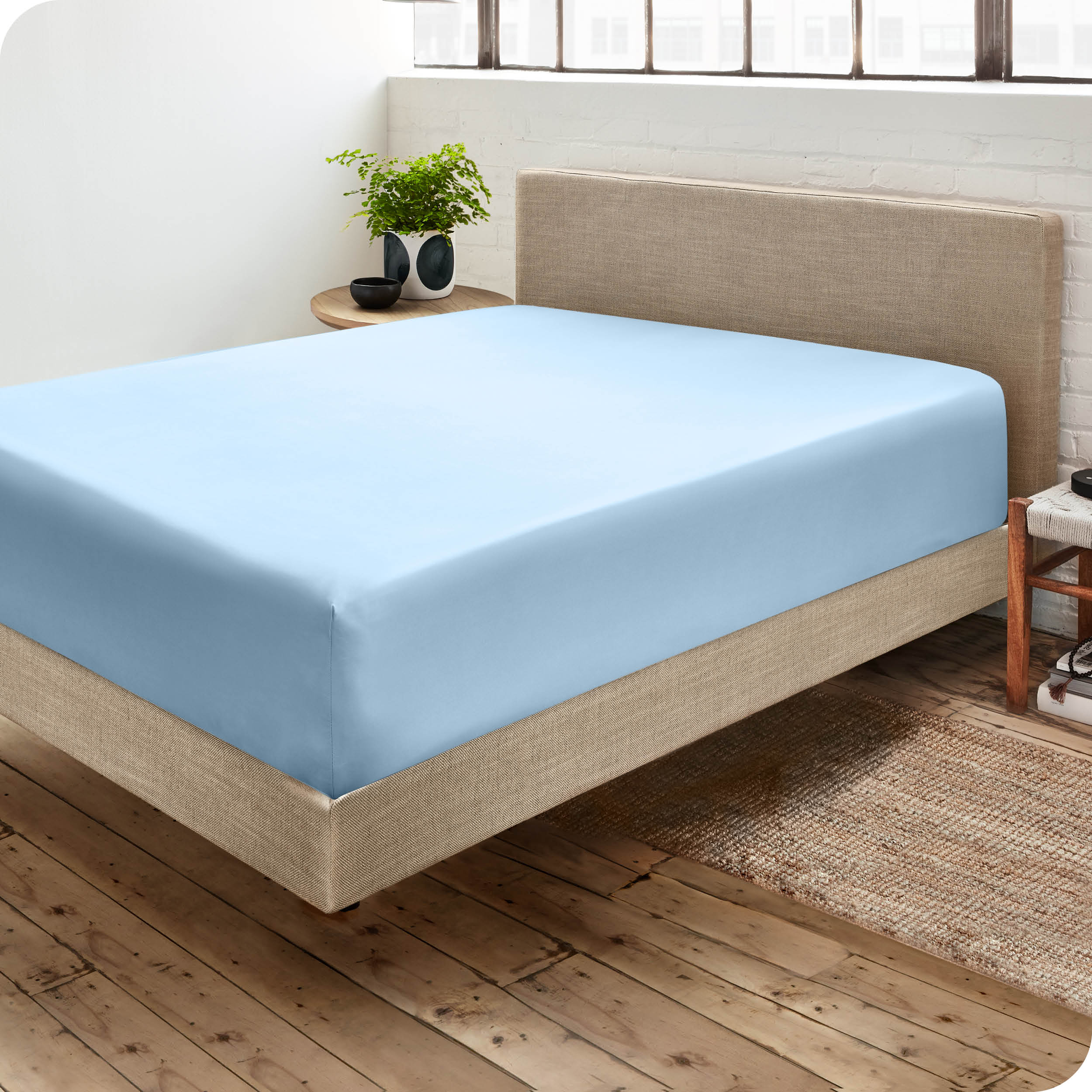 Corner view of a modern bed with a microfiber fitted sheet on the mattress. 