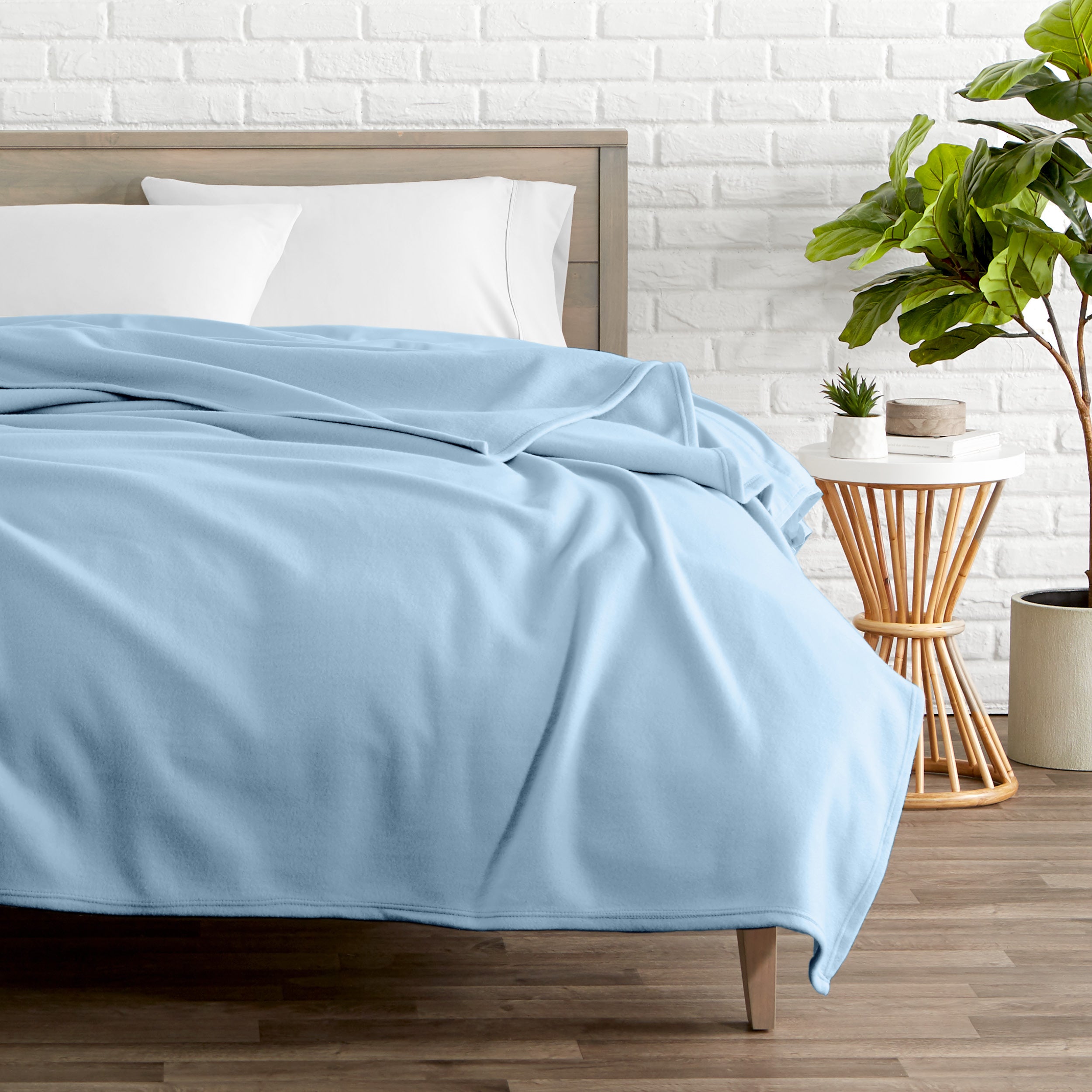 A polar fleece blanket on a bed next to a table and a large plant