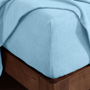 Corner of the bed with a fitted sheet on the mattress and a flat sheet draped over the side and end