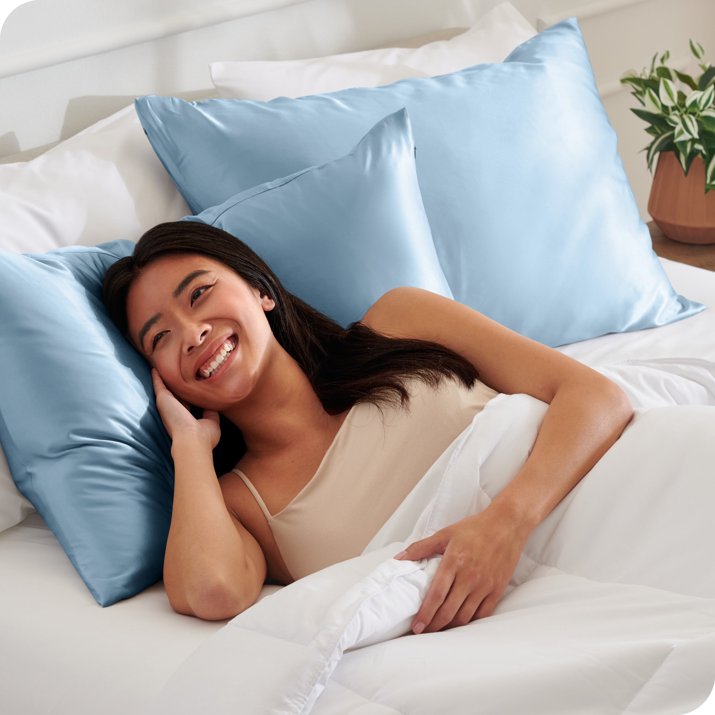 A woman in bed with her head resting on a silk pillowcase covered pillow