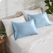 2 satin pillowcases on pillows leaning against other pillows on a bed