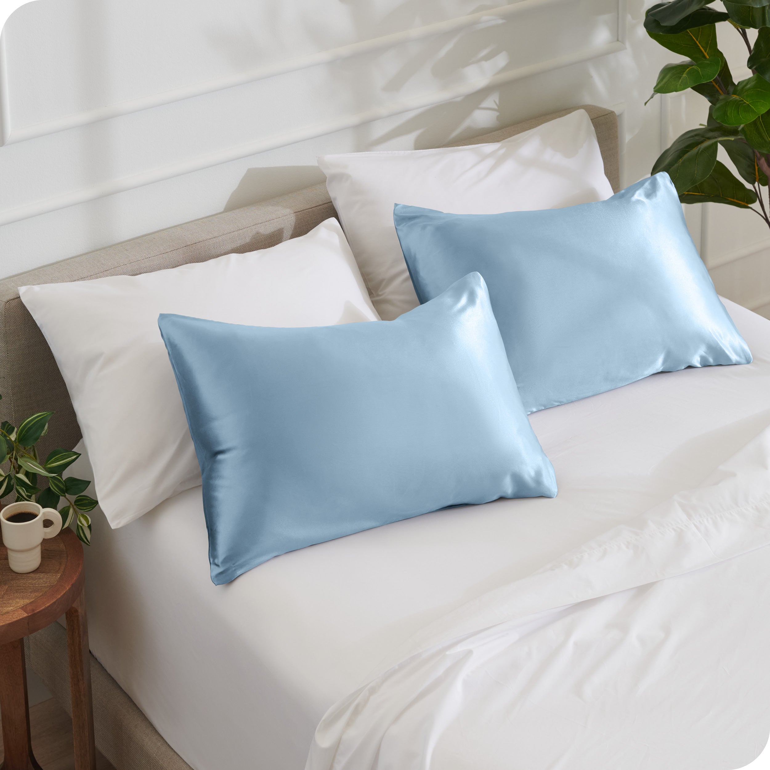 2 satin pillowcases on pillows leaning against other pillows on a bed