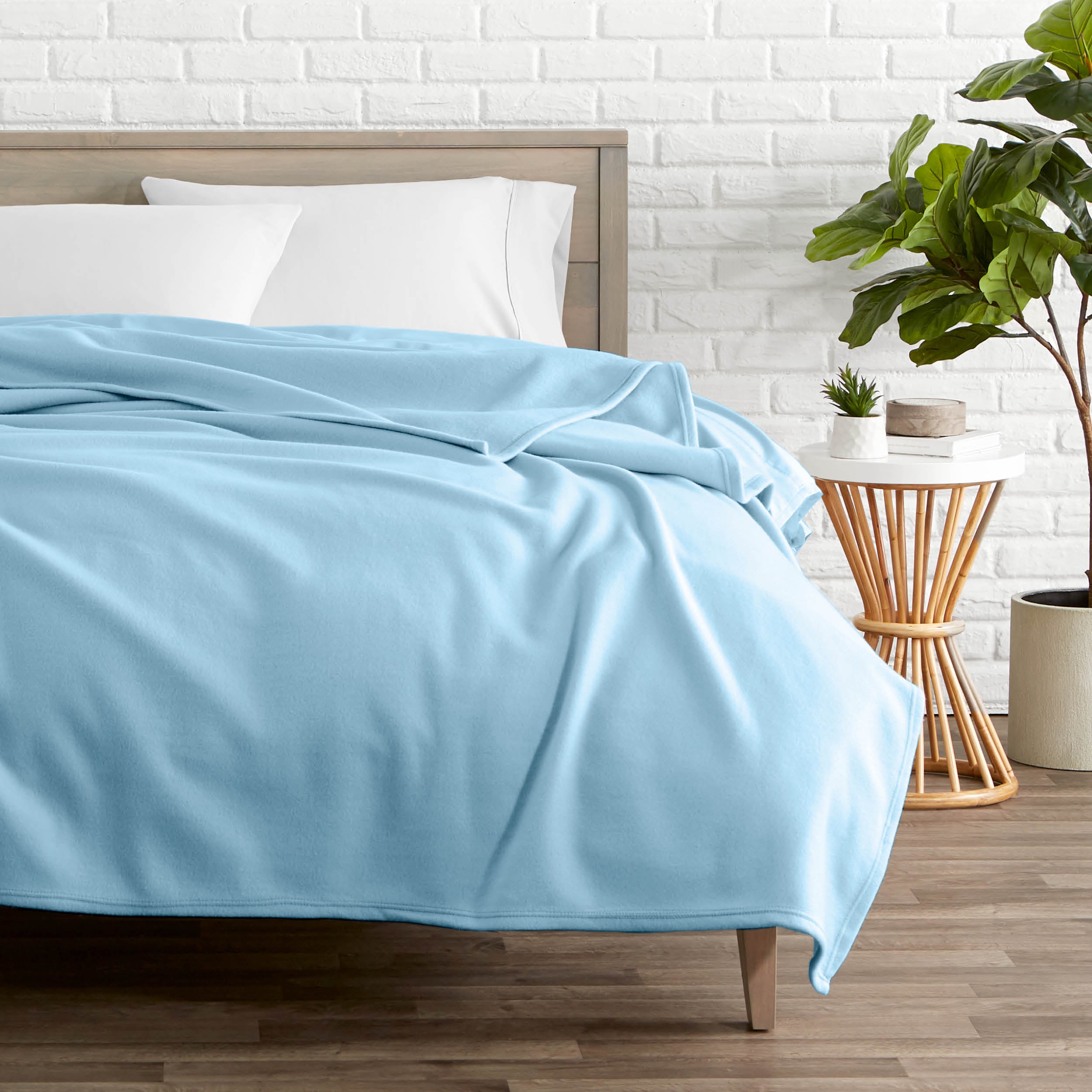 A polar fleece blanket on a bed next to a table and a large plant
