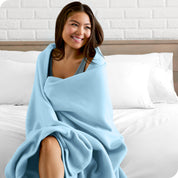 A woman sitting at the end of a bed with a fleece blanket wrapped around her shoulders