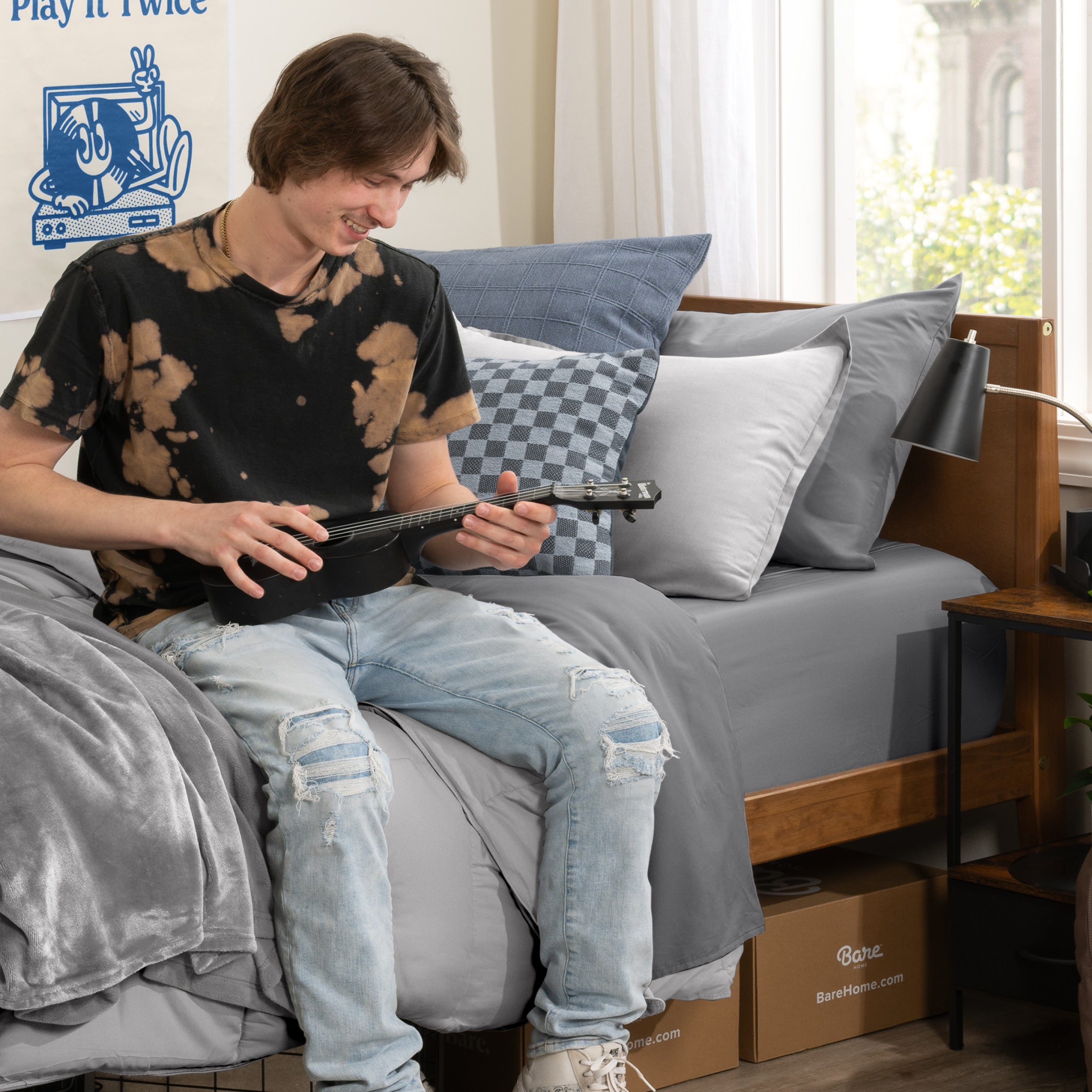 A college student sitting on his bed play a guitar