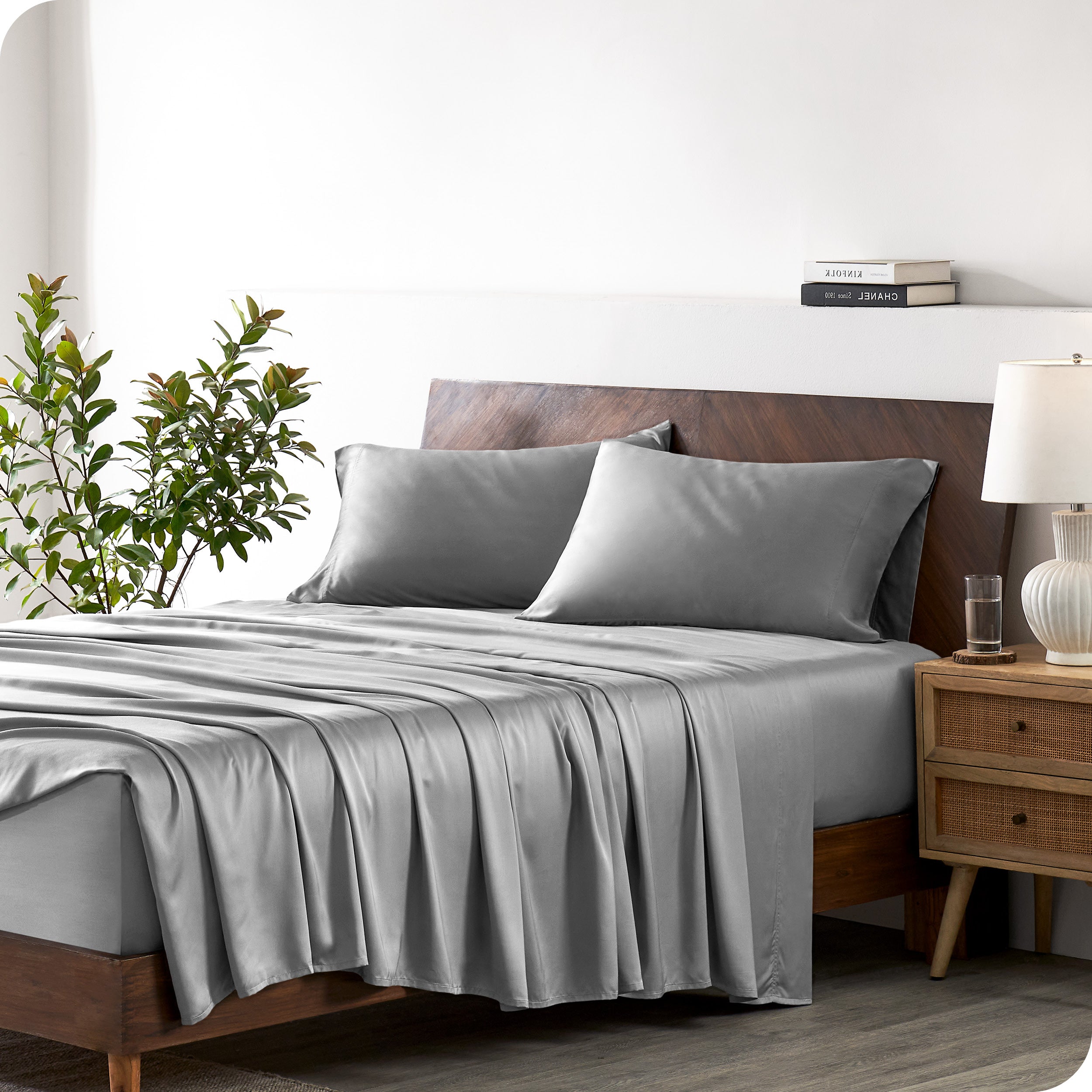 Modern bedroom with a bed against a white wall with a nightstand next to the bed. The bed has bamboo sheets draped over it.