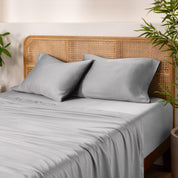 Bamboo bed sheets and pillowcases on a bed with a wicker headboard and plants in the background.