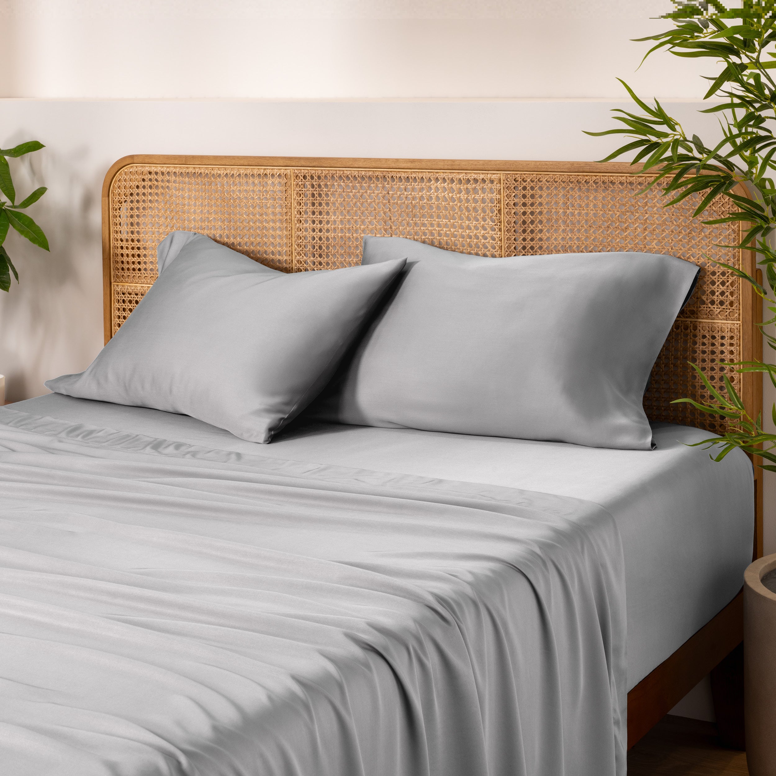 Bamboo bed sheets and pillowcases on a bed with a wicker headboard and plants in the background.