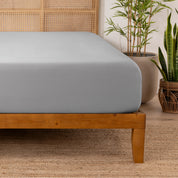 Bamboo fitted sheet on a wooden bed with plants in the background