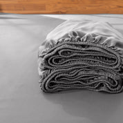 Folded fitted sheet on a bed with a wooden headboard.