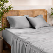 Bamboo bed sheets and pillowcases on a bed with a wicker headboard in a room with plants.