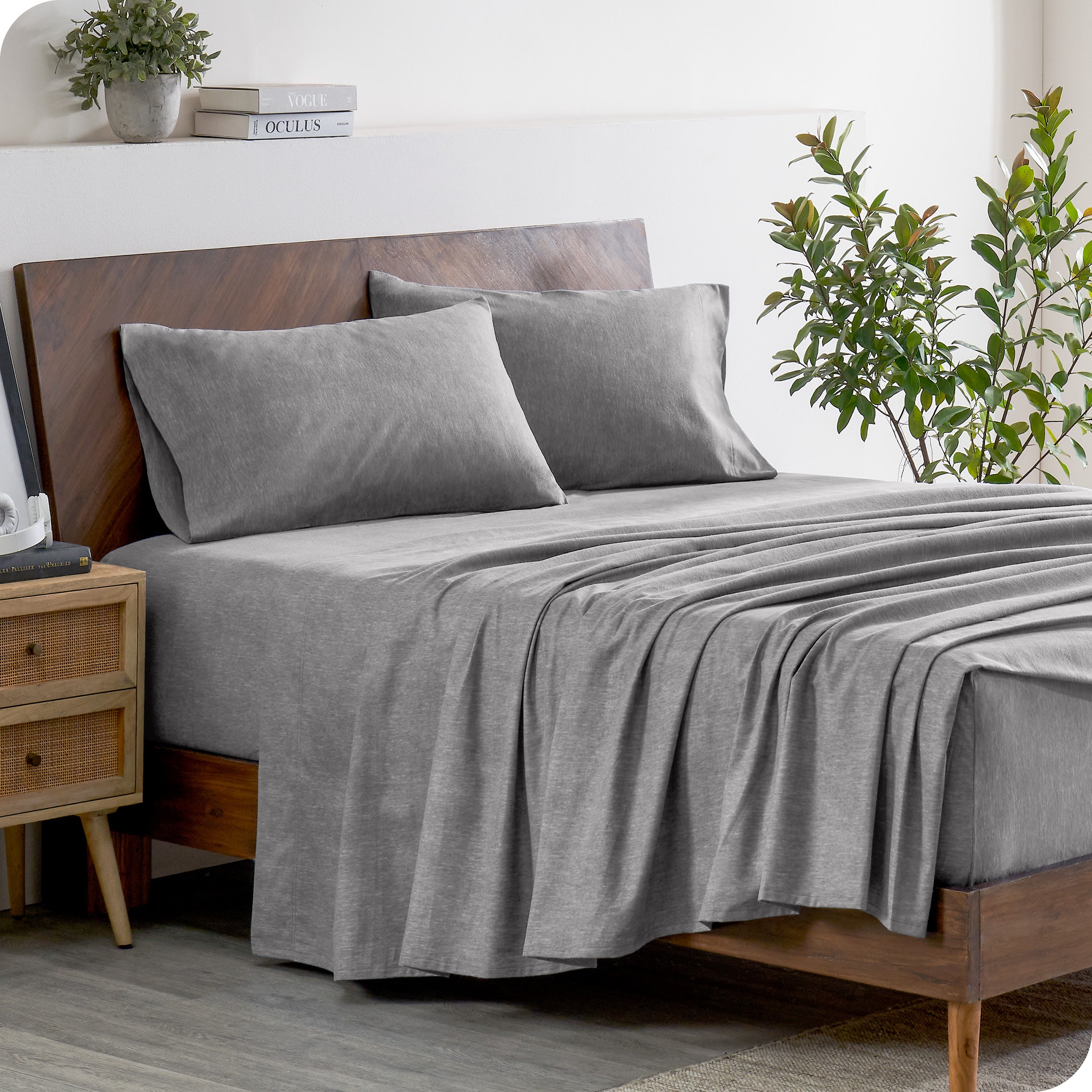 A wooden bed frame with heathered flannel sheets and pillowcases on the mattress