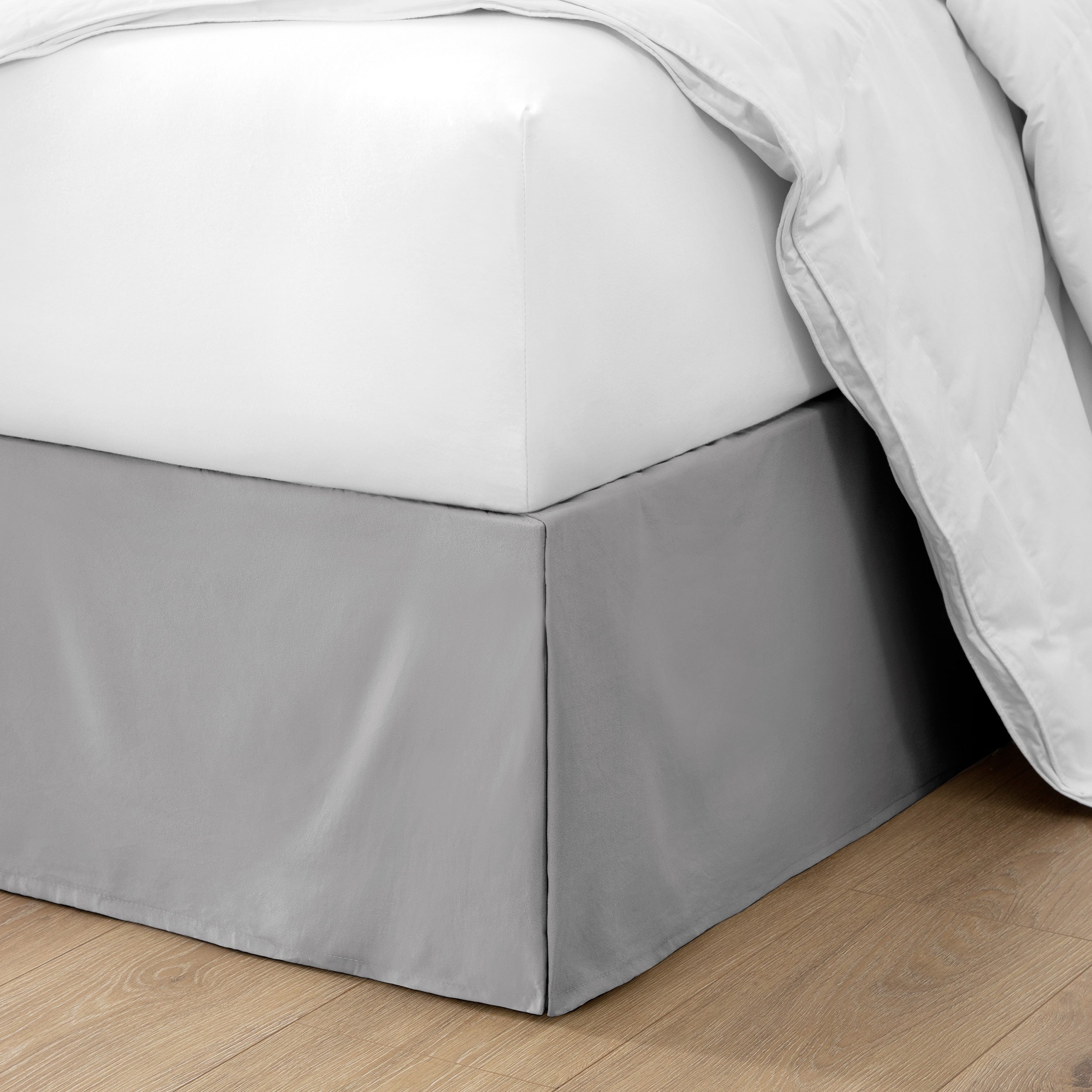 The corner of a bed with a bed skirt and comforter on it