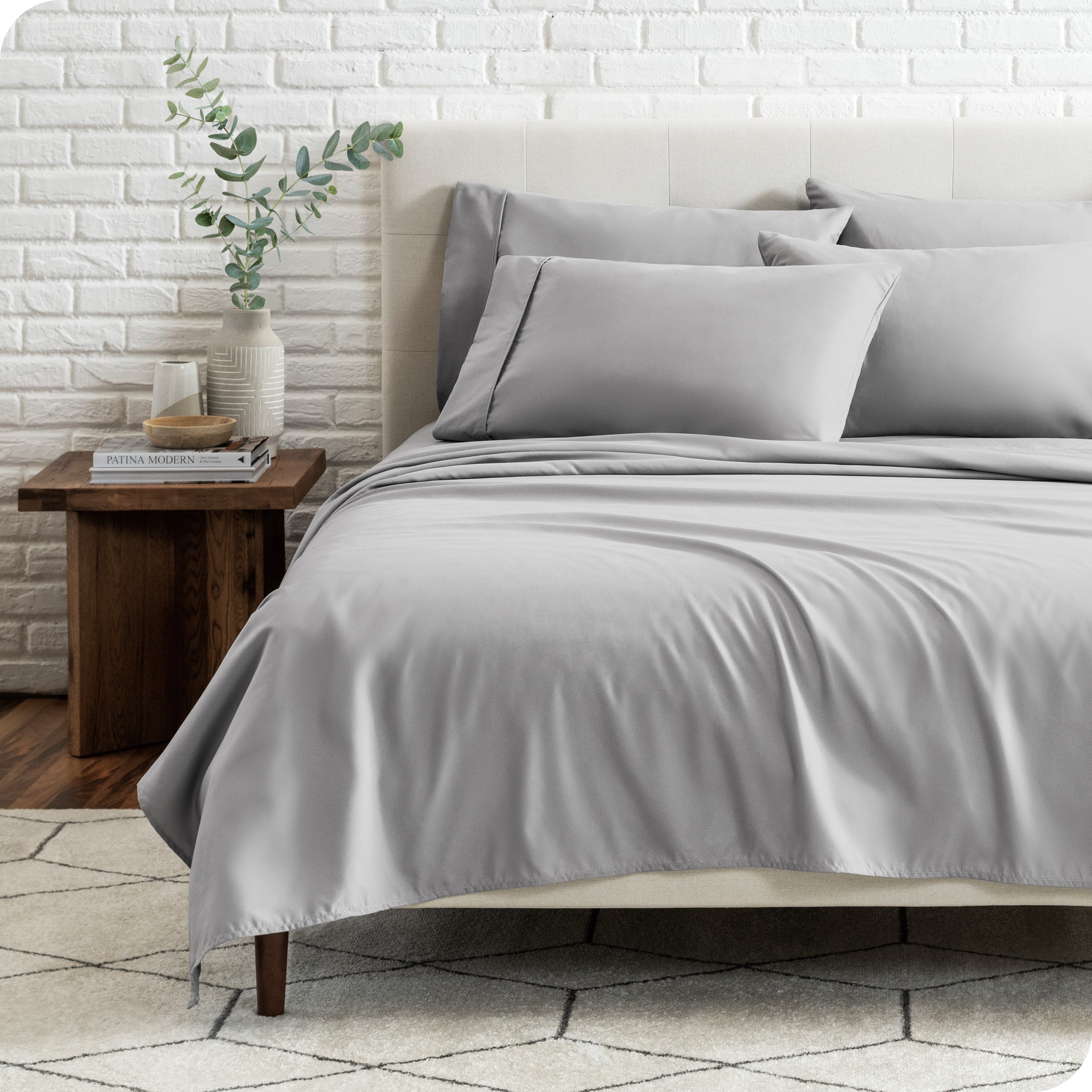 End view of a modern bed with the microfiber sheets on the bed with four pillows.