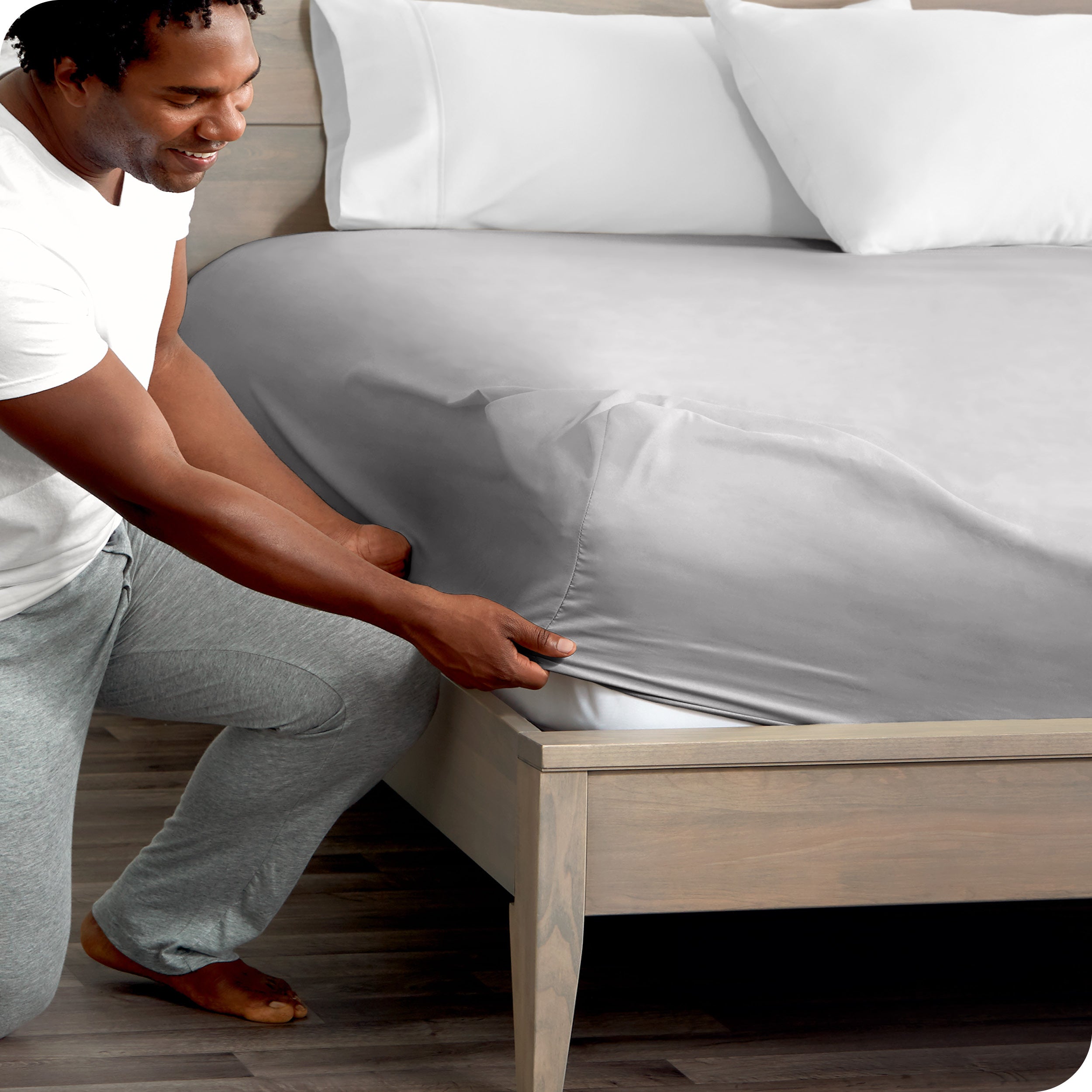 A man kneeling while putting a fitted sheet on a bed