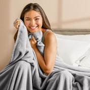A woman sitting on a bed wrapped in a microplush blanket