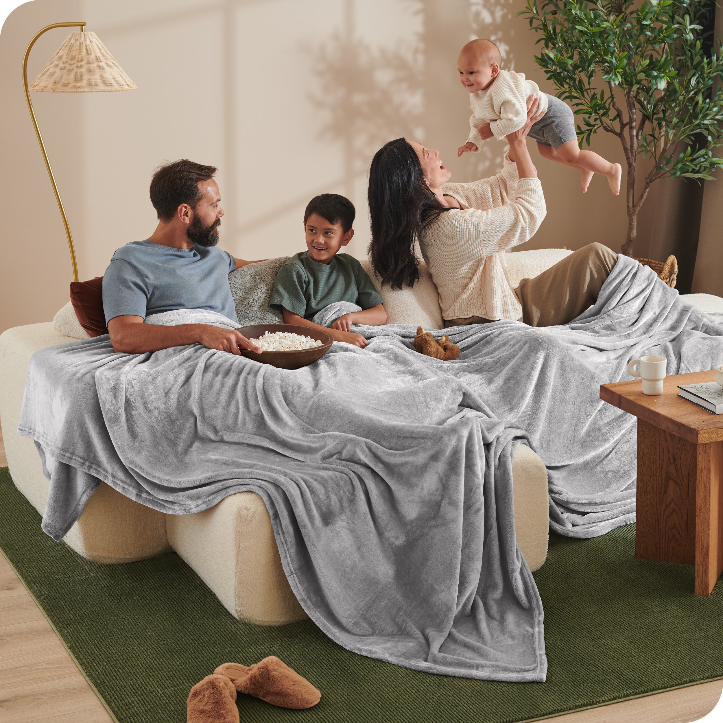 A family sitting on a couch with a giant microplush blanket covering them