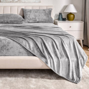 Microplush sheets on a bed in a bedroom setting with a nightstand and lamp.