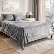 Sheets and matching pillowcases on a bed in a bedroom with a lamp and window in the background.