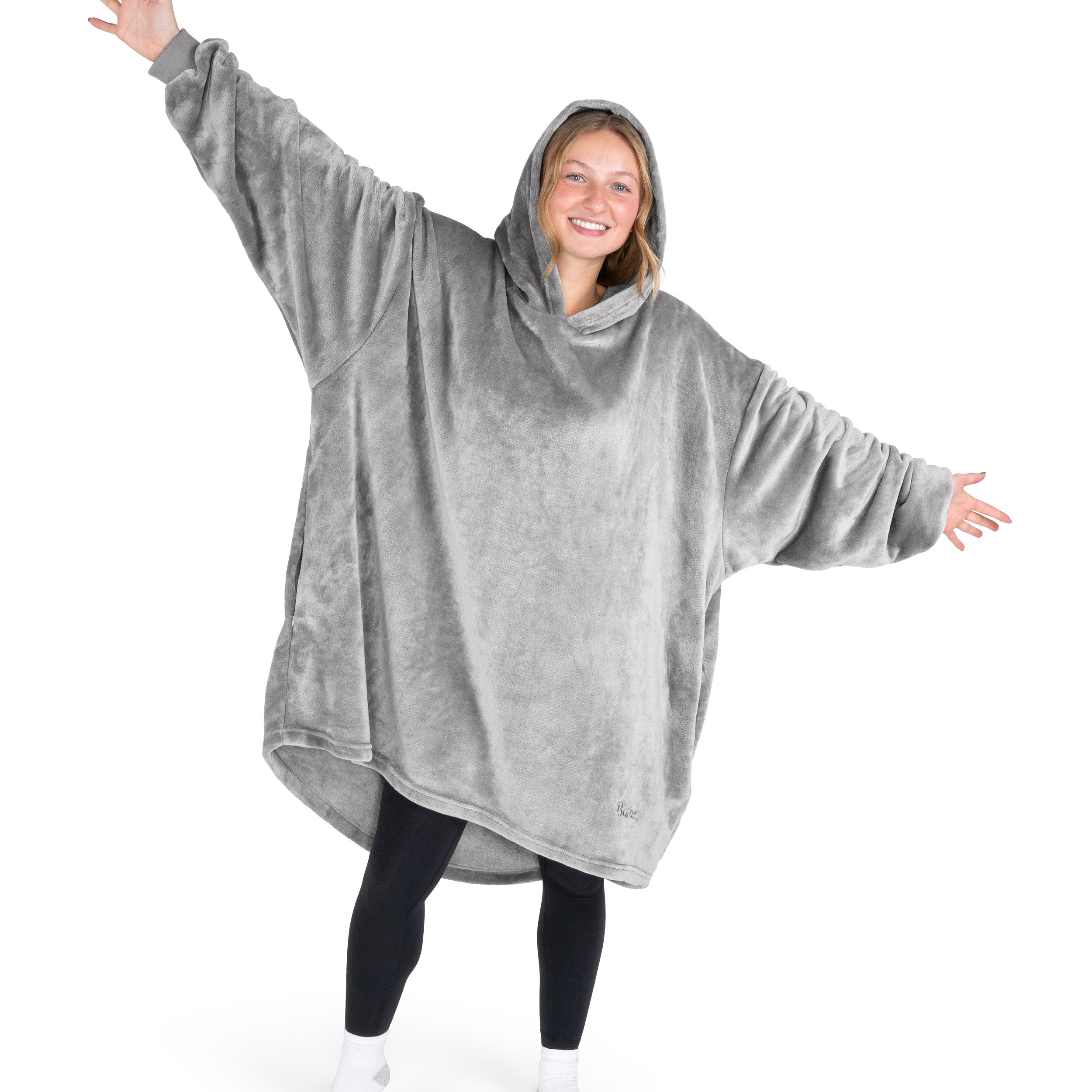 A woman is standing with her arms stretched out and has a hooded wearable blanket on