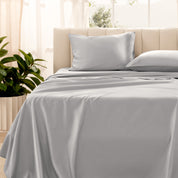 Organic sateen bedding on a bed with a beige headboard and plant in the corner.