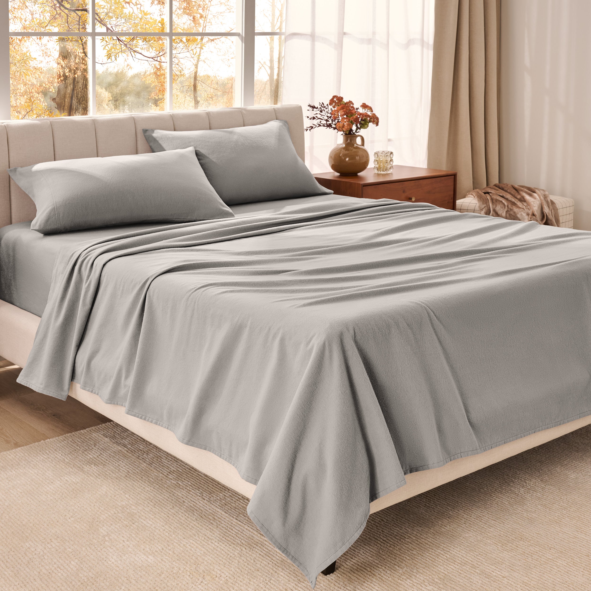 Organic flannel bed sheets on a neatly made bed in a bright bedroom with large windows.