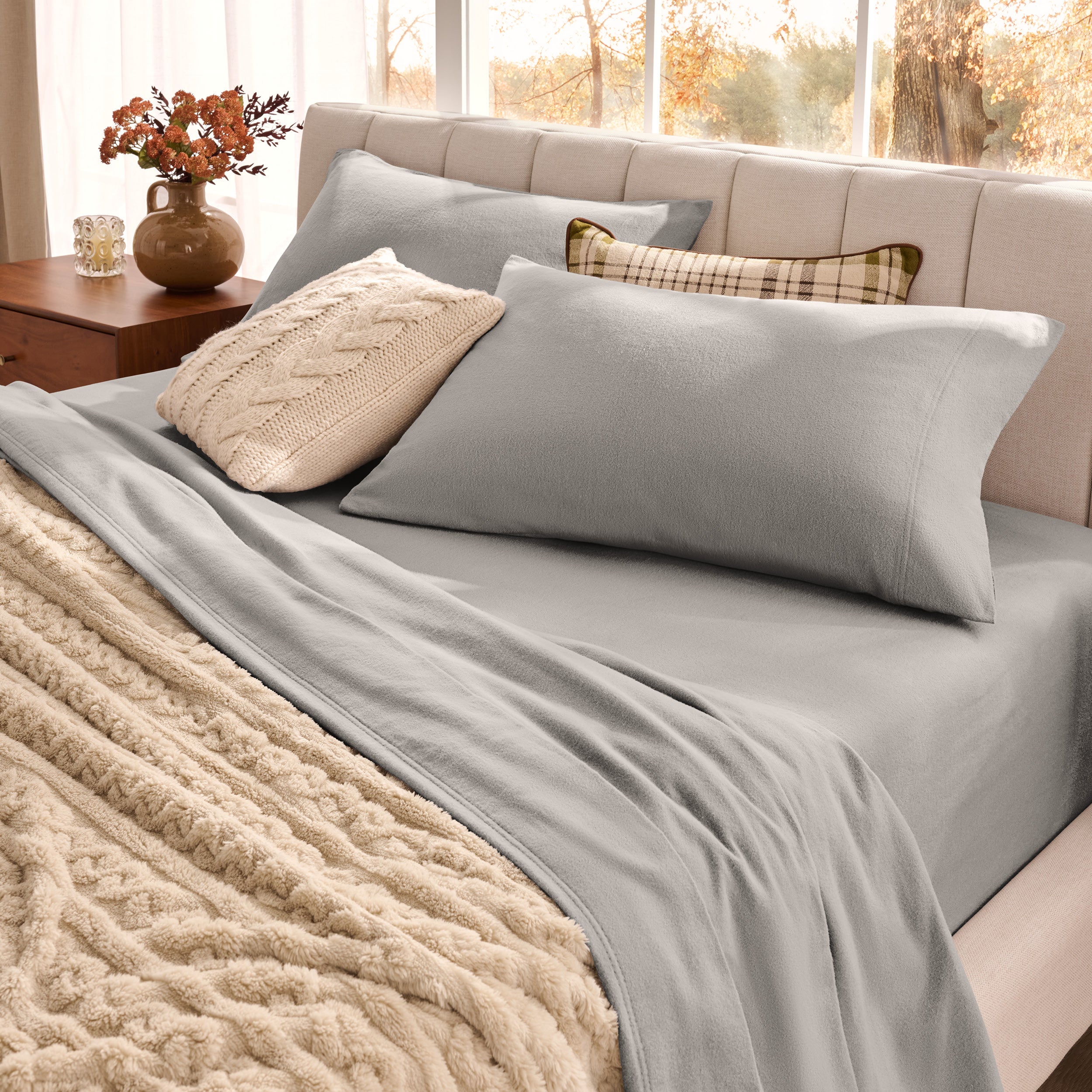 Neatly made bed with pillows and a beige blanket in a bright room.