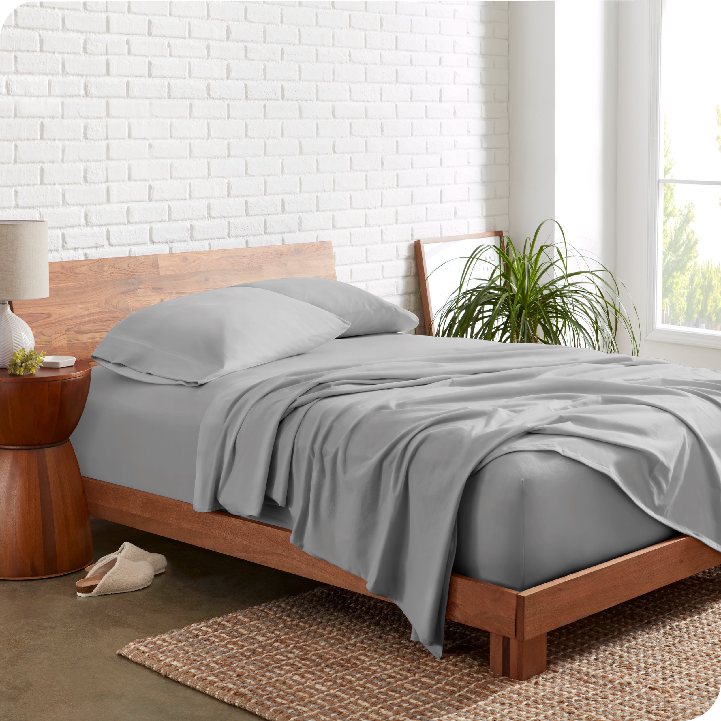 Organic jersey sheets on a bed with a brick wall behind the headboard