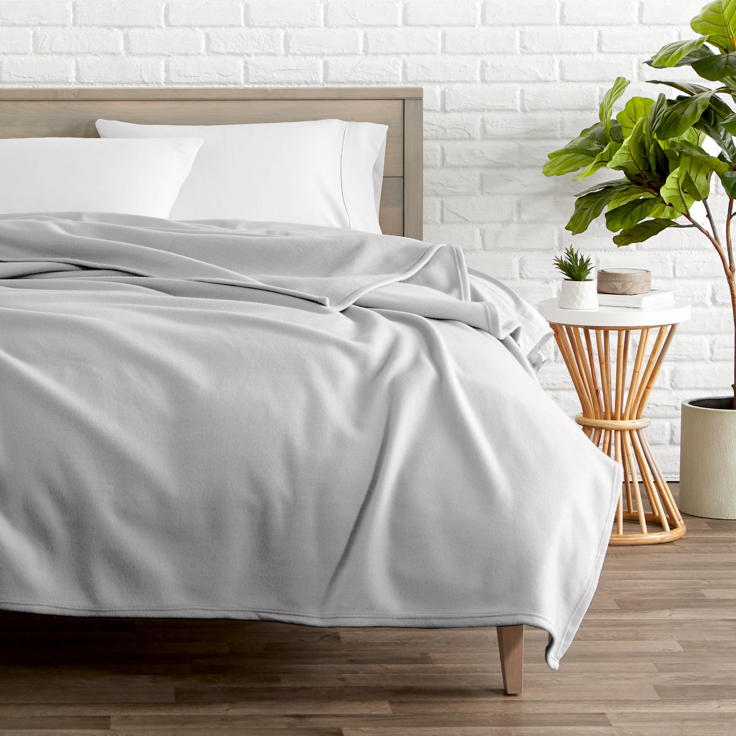 A polar fleece blanket on a bed next to a table and a large plant