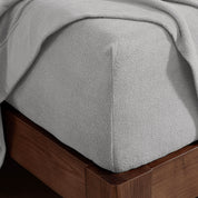 Corner of the bed with a fitted sheet on the mattress and a flat sheet draped over the side and end
