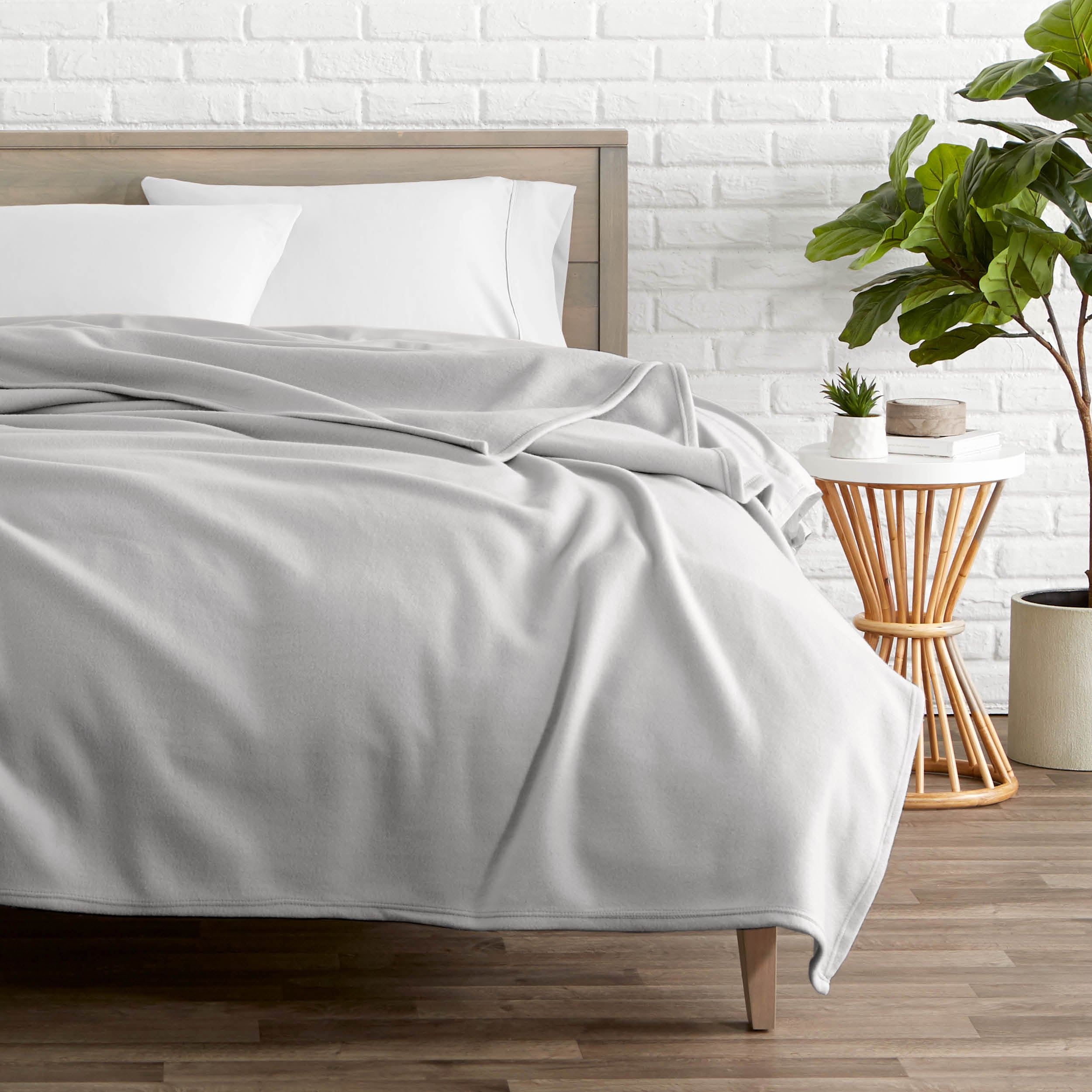 A polar fleece blanket on a bed next to a table and a large plant