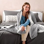 Woman cuddling with a sherpa blanket while sitting on the end of a bed
