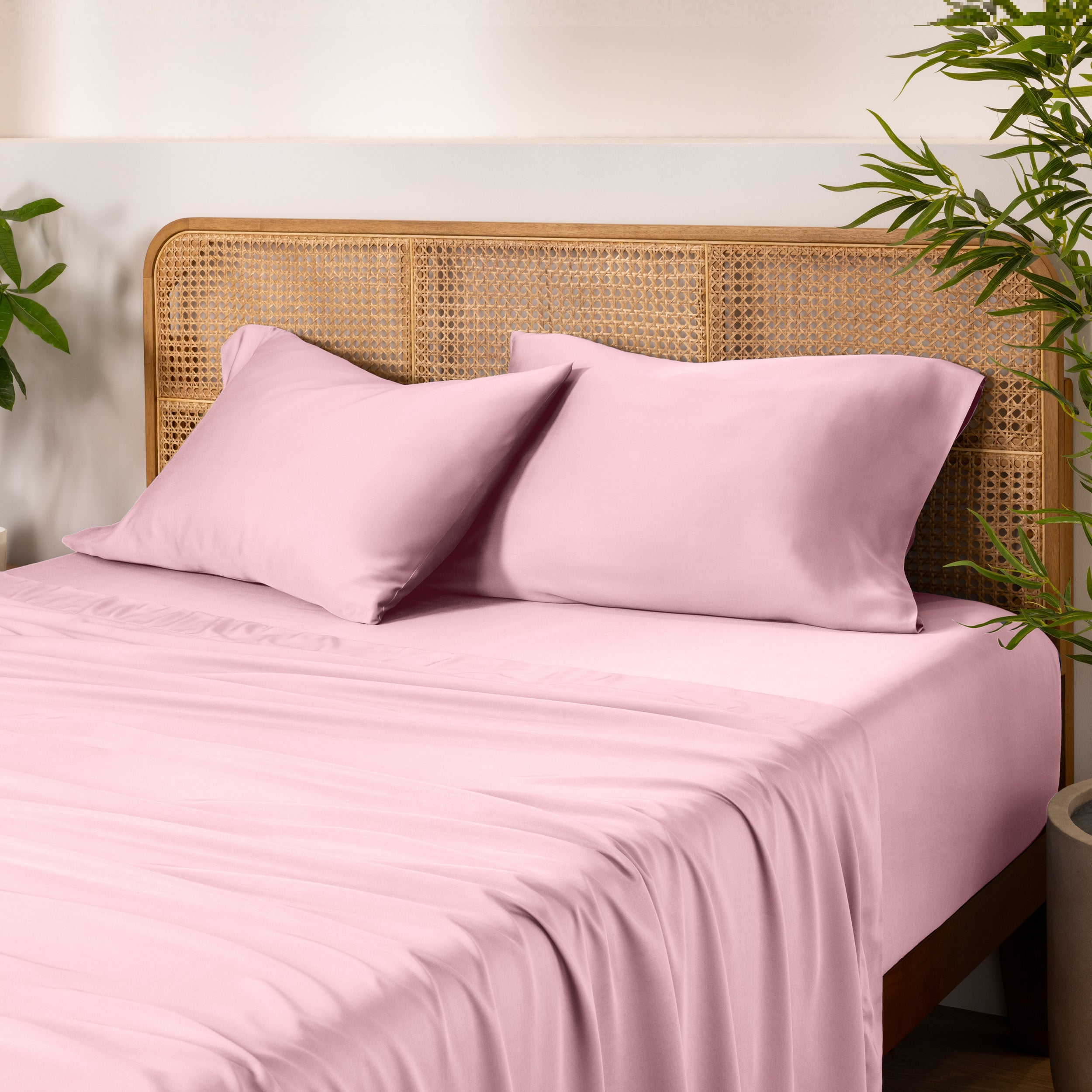 Bamboo bed sheets and pillowcases on a bed with a wicker headboard and plants in the background.