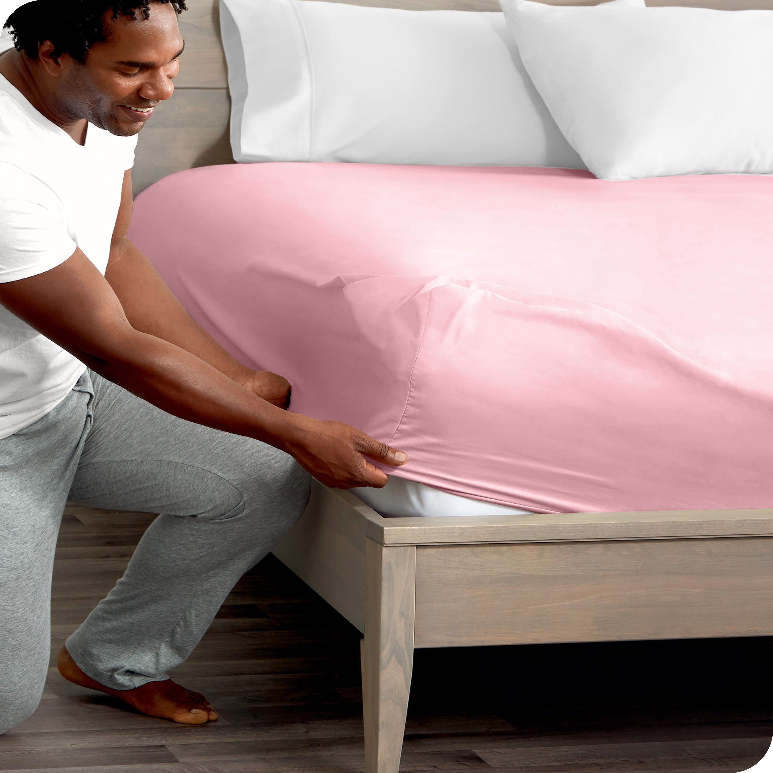 A man kneeling while putting a fitted sheet on a bed