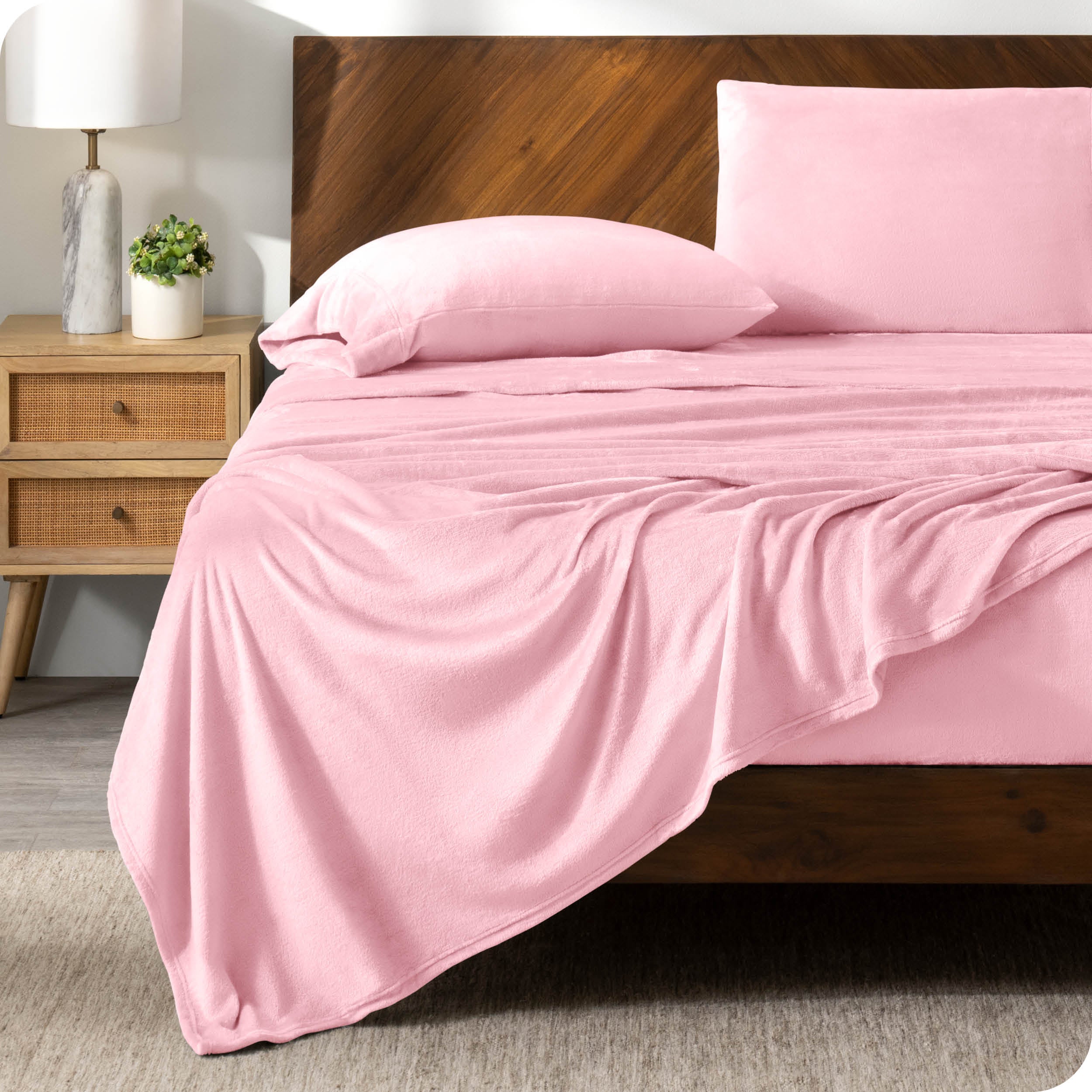 A light pink sheet set on a bed with a wooden bed frame