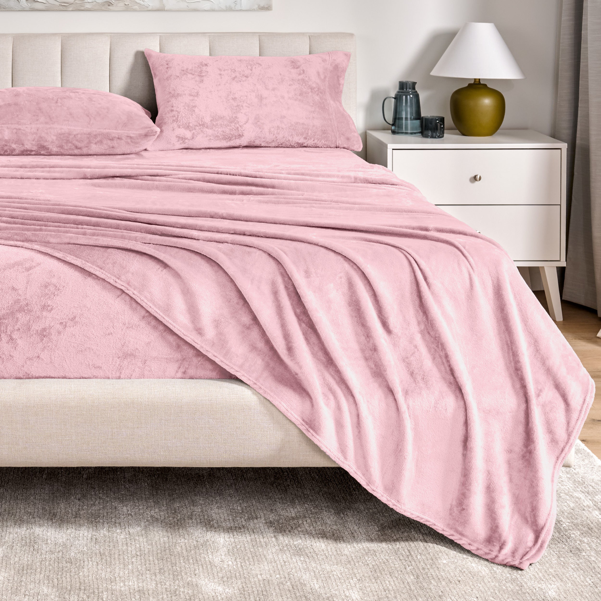 Microplush sheets on a bed in a bedroom setting with a nightstand and lamp.