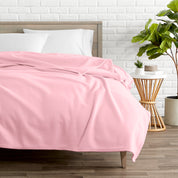 A polar fleece blanket on a bed next to a table and a large plant