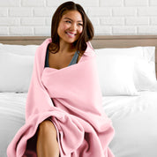 A woman sitting at the end of a bed with a fleece blanket wrapped around her shoulders