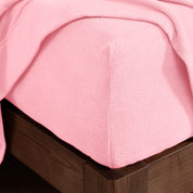 Corner of the bed with a fitted sheet on the mattress and a flat sheet draped over the side and end