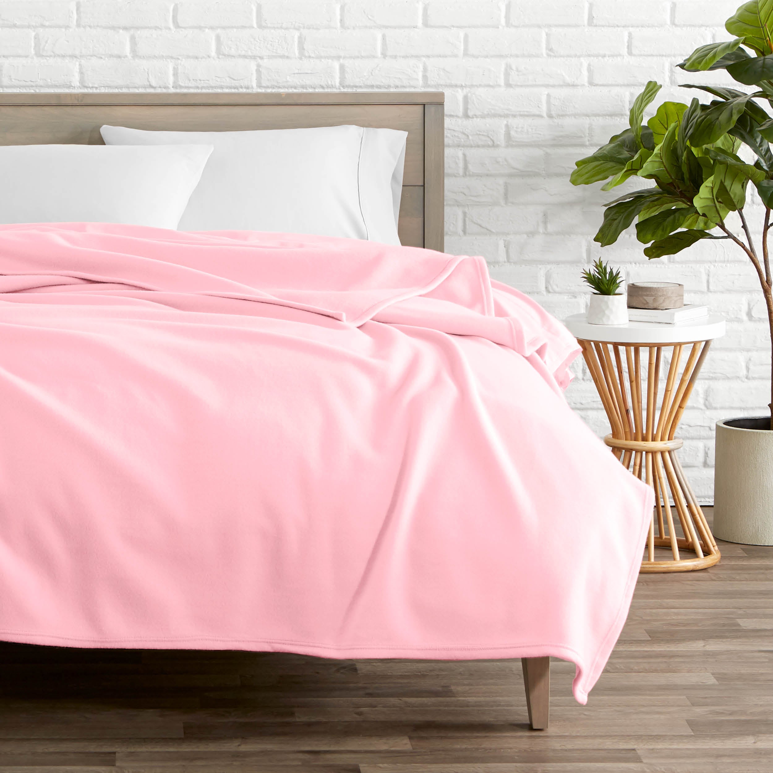 A polar fleece blanket on a bed next to a table and a large plant