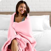 A woman sitting at the end of a bed with a fleece blanket wrapped around her shoulders