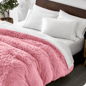 Diagonal view of a bed made with white sheets and pillowcases with a pink shaggy duvet cover on top