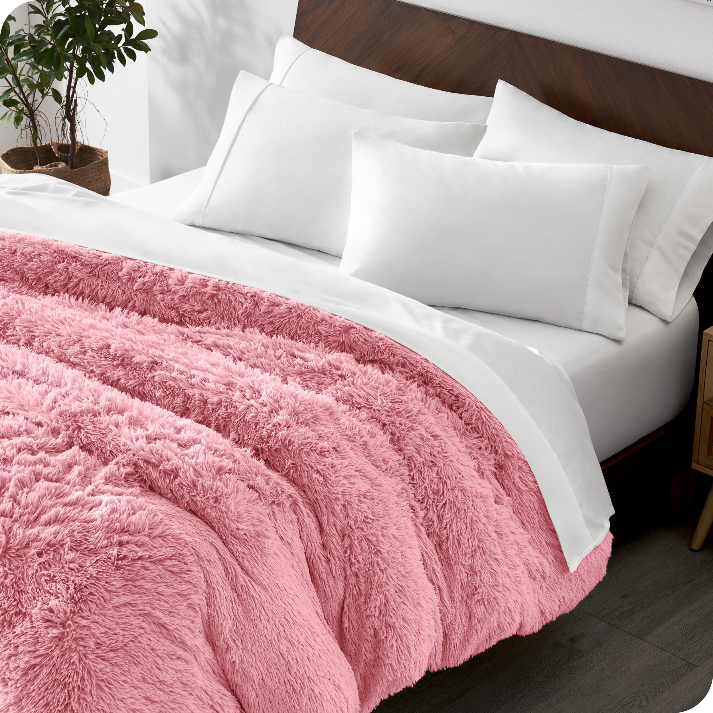 Diagonal view of a bed made with white sheets and pillowcases with a pink shaggy duvet cover on top