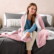 Woman cuddling with a sherpa blanket while sitting on the end of a bed