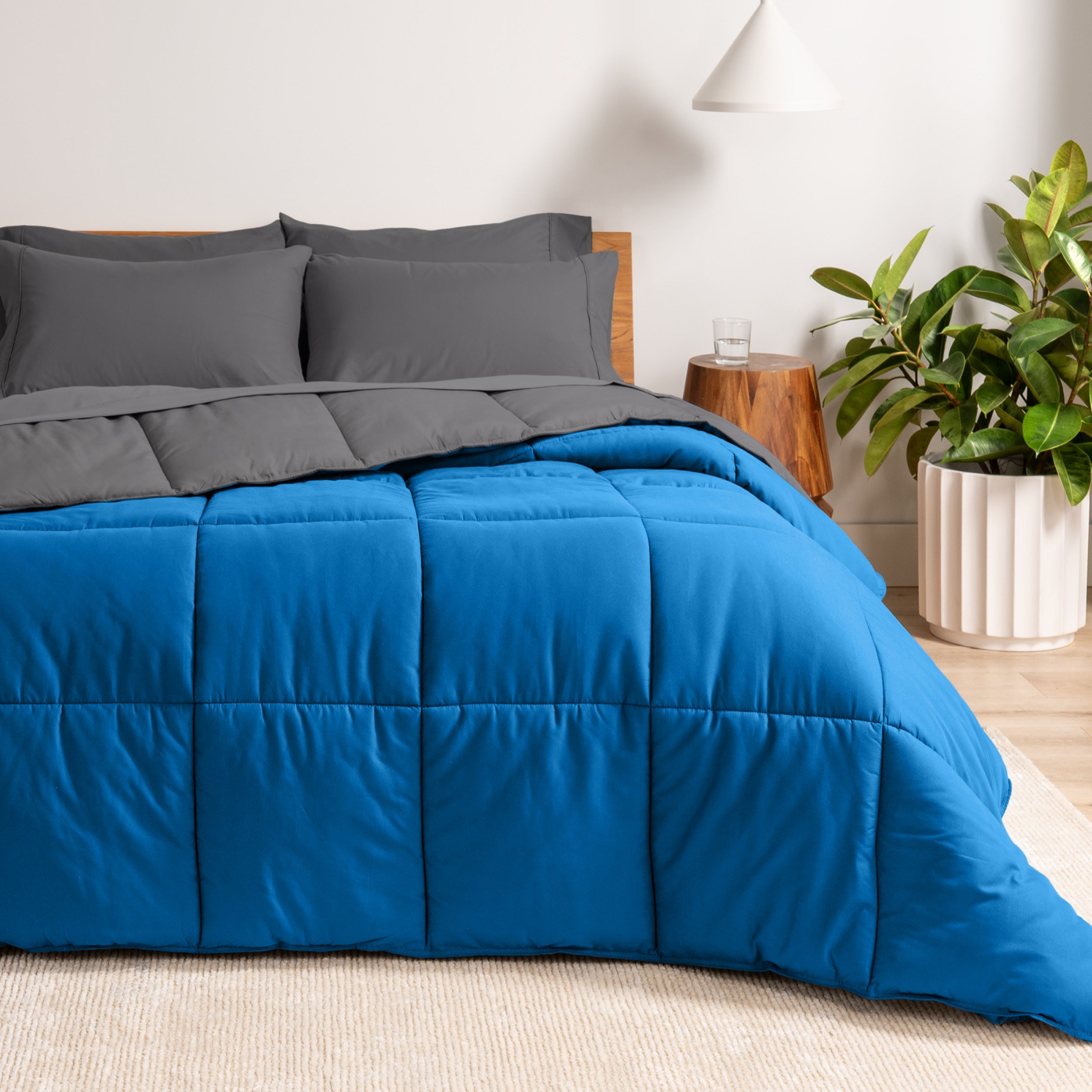 A wooden bed frame with a reversible comforter and sheet set on the mattress in a bright warm room.